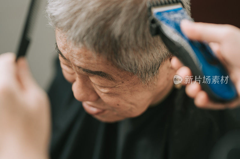an asian chinese mid adult woman is cutting and trimming hair for her father in the kitchen due to travel ban